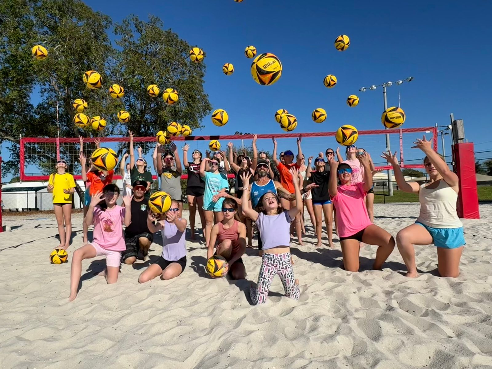 Junior beach volleyball athletes tossing volleyballs in the air at practice in Naples